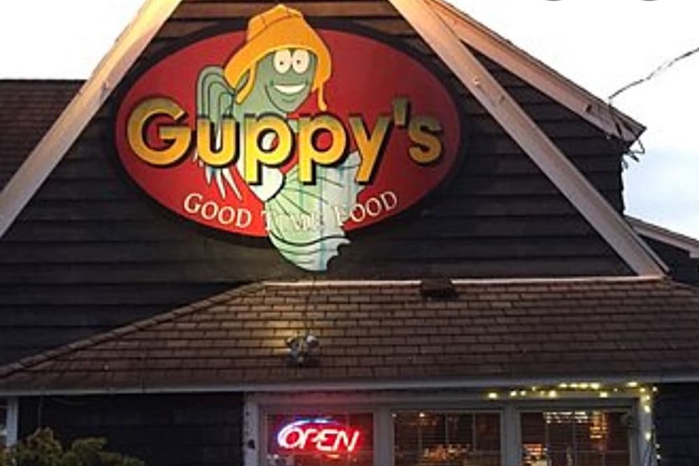 Sign for Guppy's seafood restaurant featuring a cartoon fish and "OPEN" neon light.