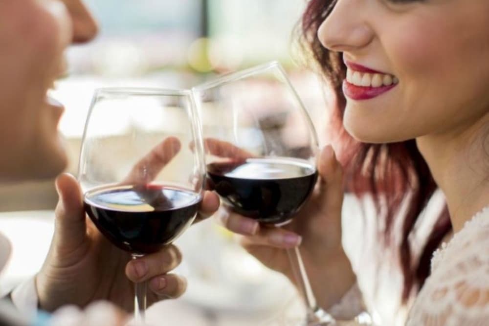 A man and woman smile at each other while toasting with glasses of red wine.
