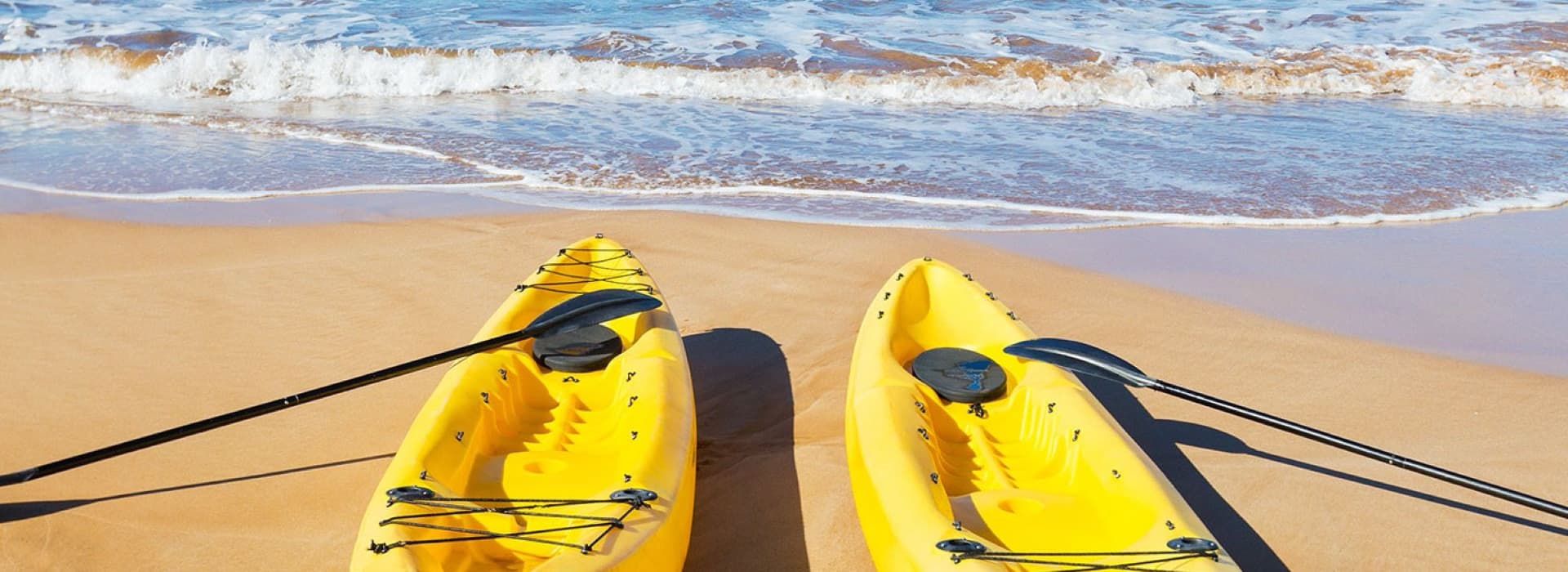 Two yellow kayaks lie on a sandy beach with gentle waves in the background.