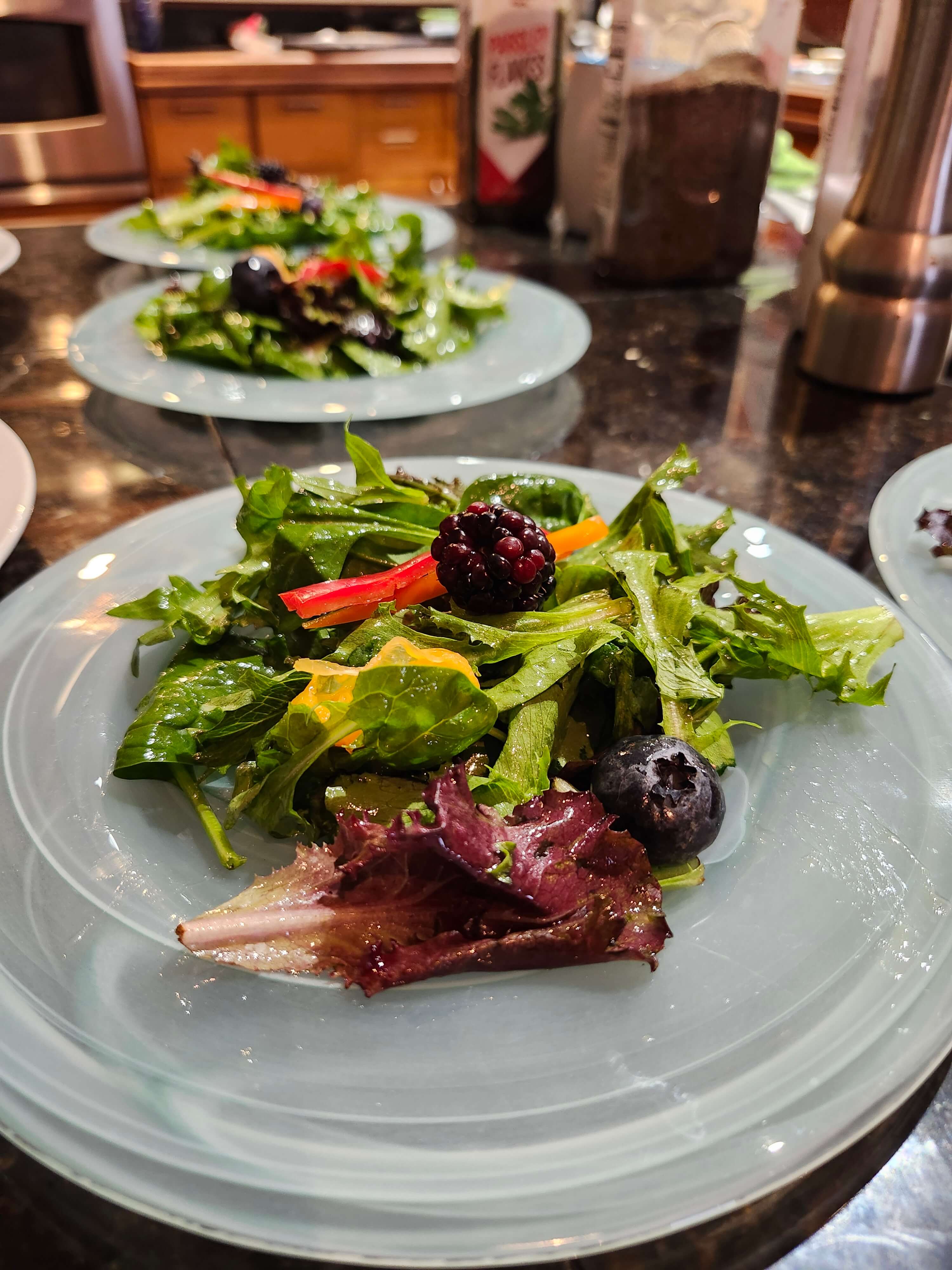 A colorful salad with mixed greens, blueberries, blackberries, and bell pepper served on a light blue plate.