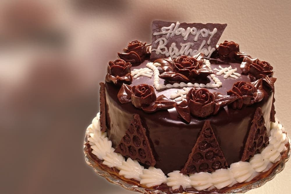 A layered chocolate birthday cake decorated with roses and the message "Happy Birthday."