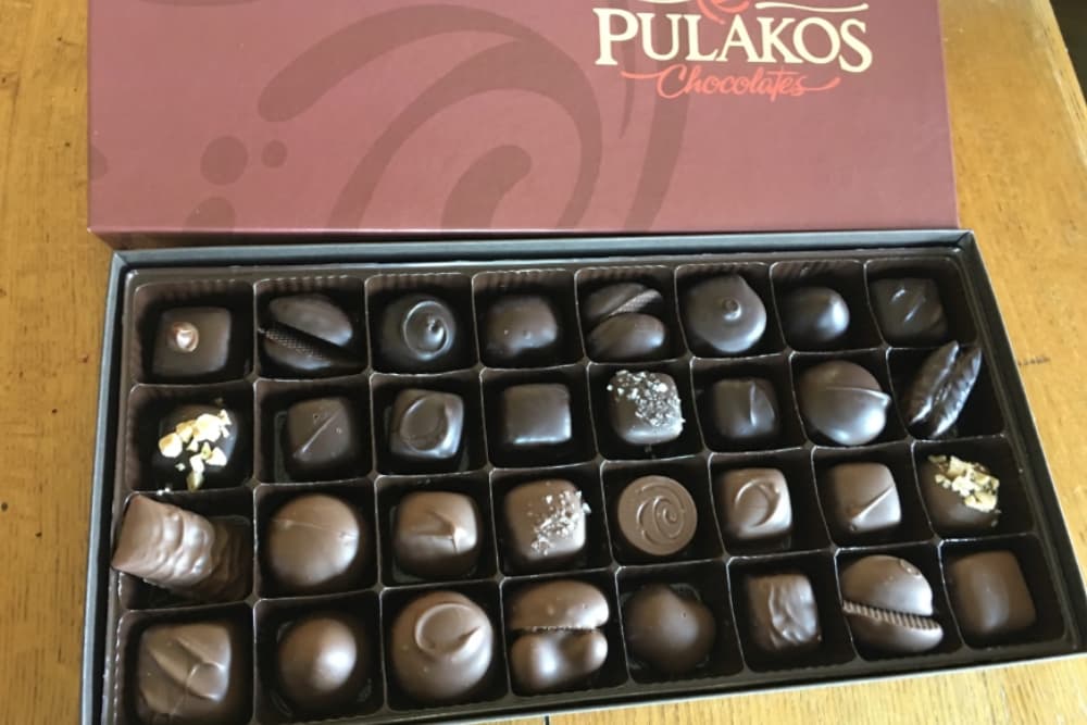 A box of assorted chocolates from Pulakos featuring various shapes and sizes.