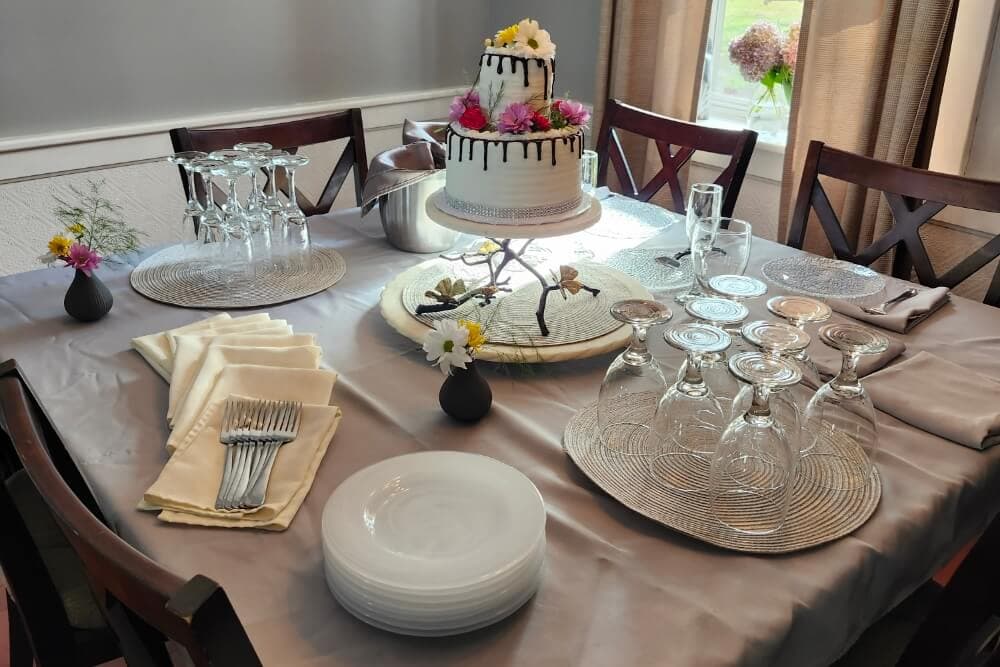 A beautifully set dining table featuring a decorated cake, elegant dishware, and glassware.