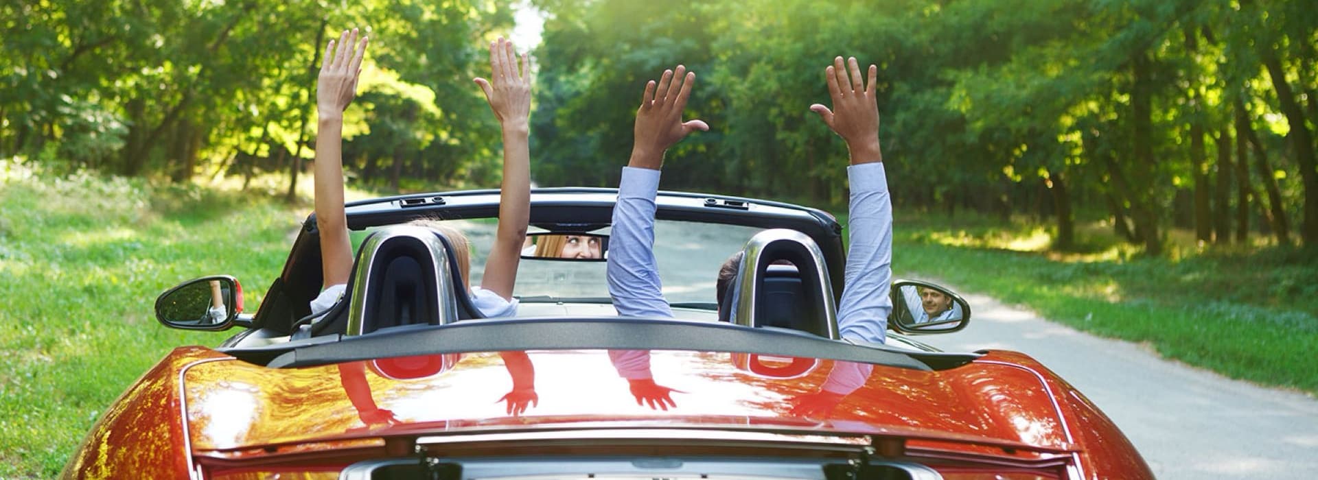 Arms raised joyfully from a convertible car driving down a tree-lined road.