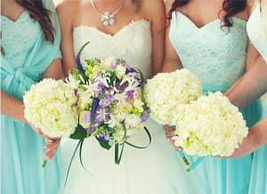 Bridesmaids in light blue dresses hold white flower bouquets alongside the bride.