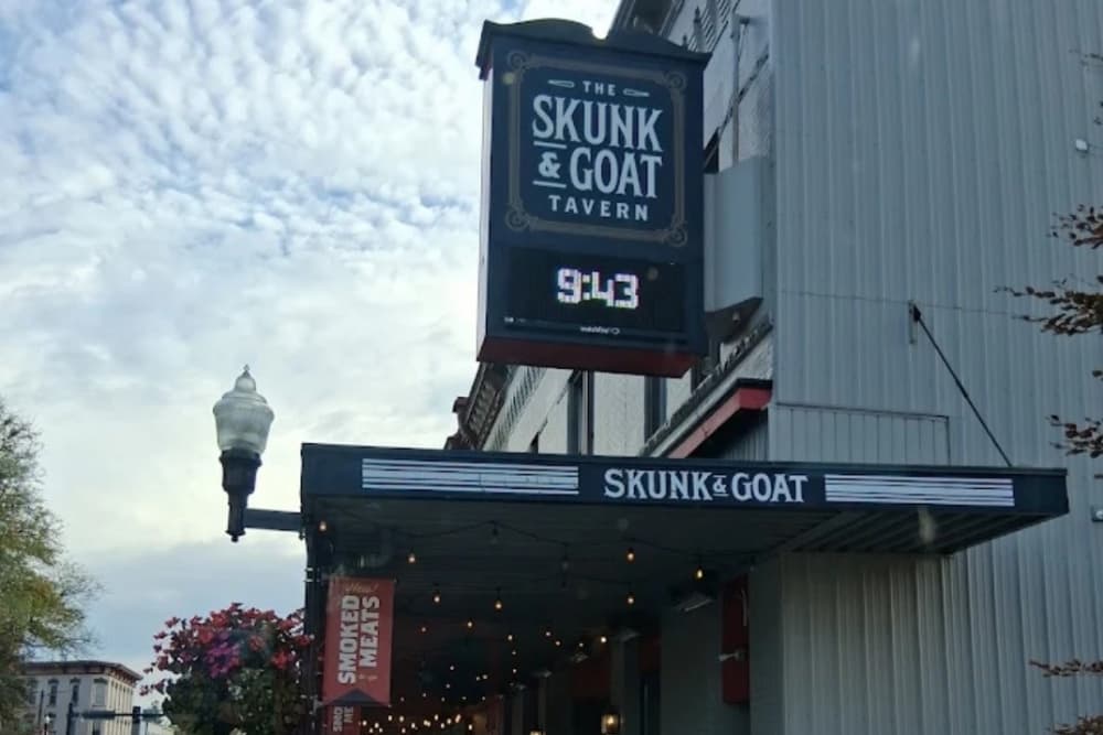 Exterior view of The Skunk & Goat Tavern with a decorative sign and outdoor seating.