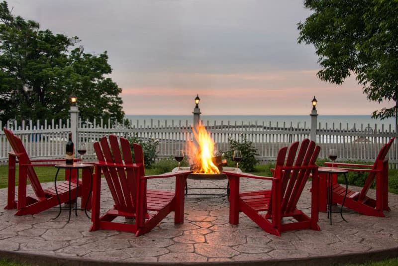 A cozy fire pit surrounded by red Adirondack chairs overlooks a serene lake at dusk. A cozy fire pit surrounded by red Adirondack chairs overlooks a serene lake at dusk.
