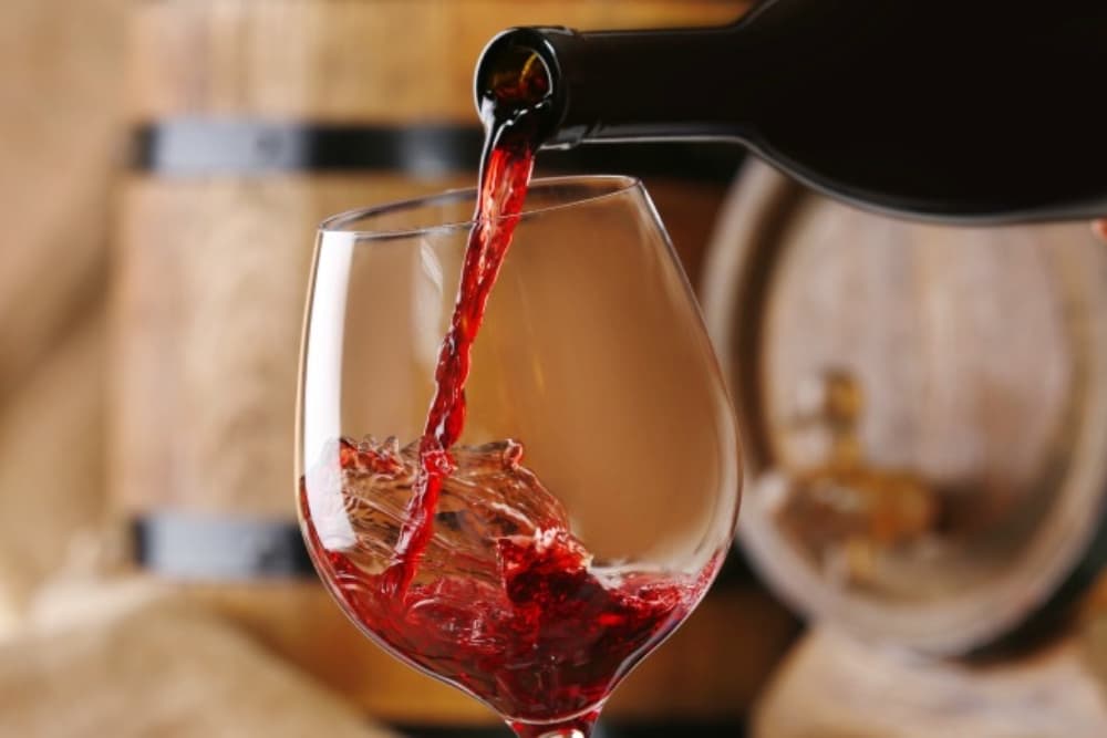 A red wine being poured into a glass, with wooden barrels in the background.