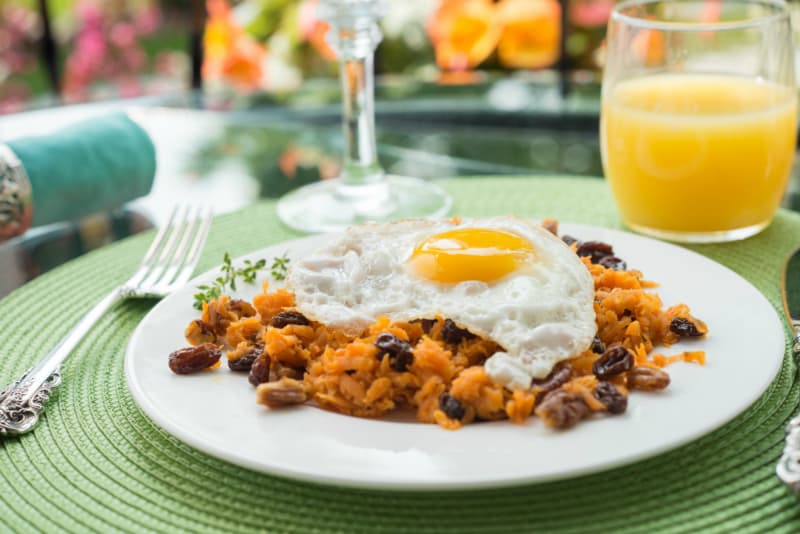 A plate of sweet potato hash topped with a fried egg, served with a glass of orange juice. A plate of sweet potato hash topped with a fried egg, served with a glass of orange juice.